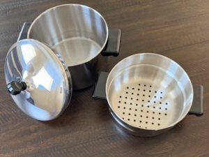 Stainless steel Farberware steamer pot with insert and lid on wooden surface