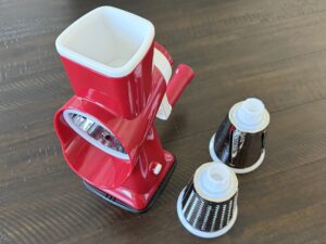Red rotary cheese grater with interchangeable blades on wooden table